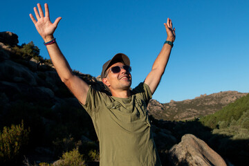 Man dressed in military green t-shirt and cap and sunglasses enjoying a day in the mountains