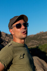 Man dressed in military green t-shirt and cap and sunglasses enjoying a day in the mountains