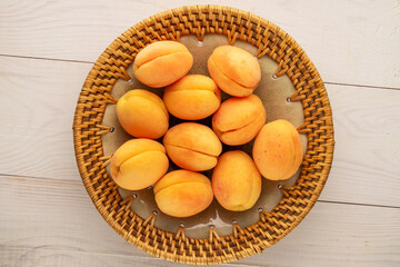 Several ripe juicy apricots in a ceramic plate on a wooden table, macro, top view.