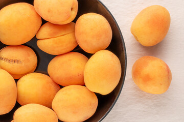 Several ripe juicy apricots in a black ceramic plate on a linen cloth, macro, top view.