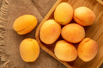 Several ripe juicy apricots with bamboo tray on jute cloth, macro, top view.