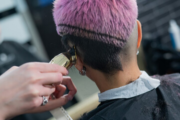 The hairdresser shaves the temple of a female client. Rear view of a woman with short pink hair in a barbershop.