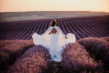 Fototapeta na wymiar Happy woman in a white dress and straw hat strolling through a lavender field at sunrise, taking in the tranquil atmosphere.