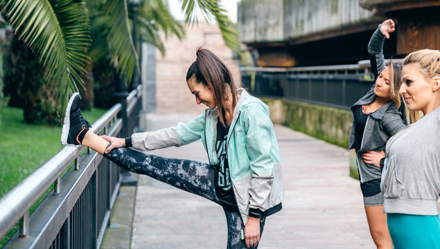 Team of three happy women friends runners stretching before training on town