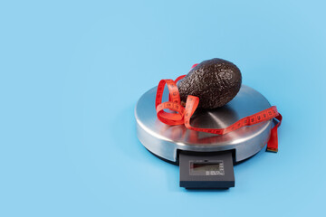 weigh food, diet and weight loss, avocado on a kitchen scales with measuring tape, blue background, copy space, calorie counting,