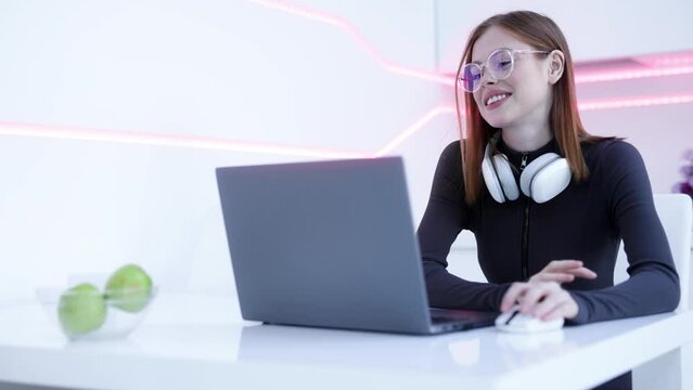 Gamer girl works and plays at the computer. Female in modern headphones interacting with network while having virtual reality experience. Augmented reality game, future technology, AI concept. VR. 