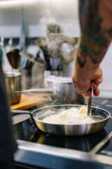 man chef cooking tasty scrambled eggs in frying pan on kitchen