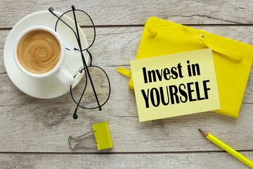 yellow notepad cup of coffee. words on sapis invest in yourself - obrazy, fototapety, plakaty