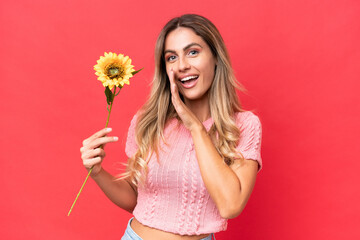 Young pretty Uruguayan woman holding sunflower isolated on background whispering something