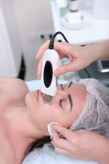 Beautiful woman receiving ultrasound cavitation facial peeling. Cosmetology and facial skin care. Ultrasonic facial cleansing. Facial cleansing by ultrasound. Vertical photo.