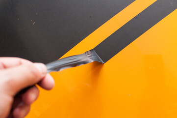 Removing black strips of stickers from the hood of a car. Removal of fast lanes. - obrazy, fototapety, plakaty