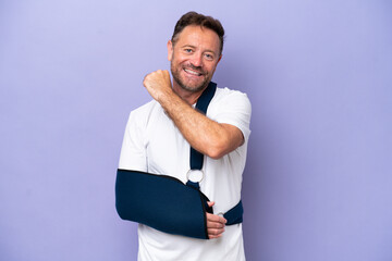 Middle age caucasian man with broken arm and wearing a sling isolated on purple background...