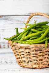Fresh green pepper in a wicker basket over wooden background. Green chili pepper harvest season concept. Vegetables for a healthy diet. Close up