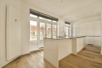 an empty kitchen with wood flooring and white cupboards on either side of the room, there is a large window in the