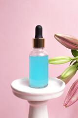 Glass dropper bottle on podium with lily flowers on pink background. Hyaluronic acid oil, serum...