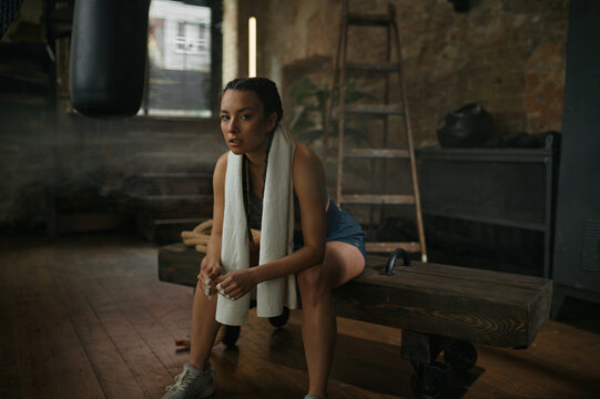 Relaxed woman boxer resting on bench with towel on neck - Powered by Adobe