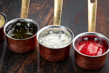 Three sauces for dishes in metal bowls close-up on a wooden table, view from the top