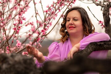 Woman peach blossom. Happy curly woman in pink dress walking in the garden of blossoming peach trees in spring