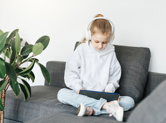 Little girl with headphones and tablet  at home