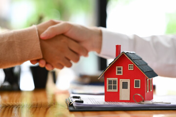 A small house model on wooden table, realtor or landlord shaking hands with client after sign agreement or sale purchase contract