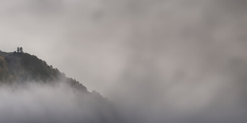 landscape, mountain peaks through clouds, light grey sky, space for text on right.