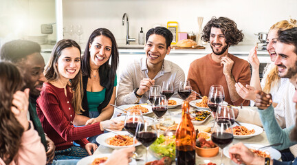Fototapeta na wymiar Happy multiethnic friends eating spaghetti or noodles with tomato sauce and drinking red wine at home during a amazing dinner party - Conviviality concept with bright warm filter