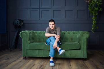 Obraz premium A handsome young boy is sitting on the sofa in the studio. Stylish loft-style interior.