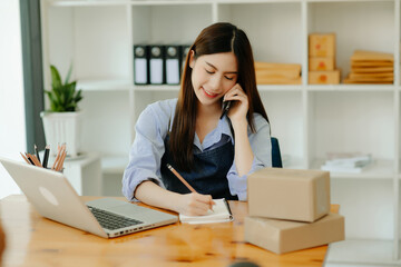 Portrait of Asian young woman SME working using smartphone or tablet taking receive and checking online purchase shopping order to business online concept.