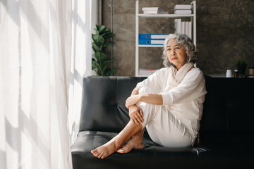 Old woman sit Depression haired  pensive glance Standing with bottle pills and pills by window  Copy space.