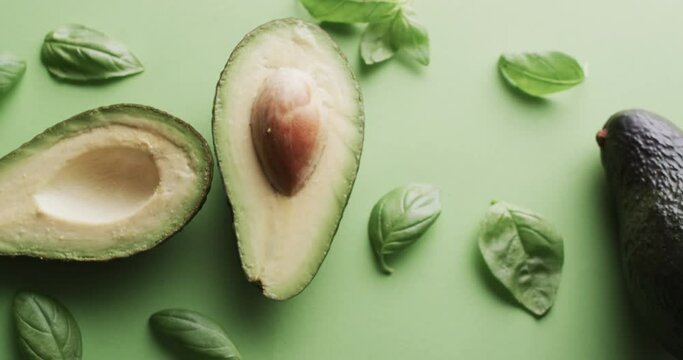 Video of sliced avocado and basil leaves with copy space over green background