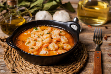 Black casserole dish with garlic prawns, or Pil-pil, on a rustic wooden table, close-up.