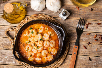 Black casserole dish with prawns al ajillo or Pil-pil, ready to eat, on a rustic wooden table, top view.