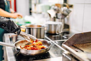 woman chef cooking chicken wings in a sauce in the kitchen