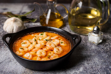Black casserole dish with garlic prawns or Pil-pil, in the background the ingredients for its preparation. Close-up.