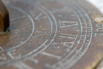 Fototapeta na wymiar Close up detail of an old metal sun dial with roman numerals and compass point directions. Narrow depth of field to create a more abstract image.