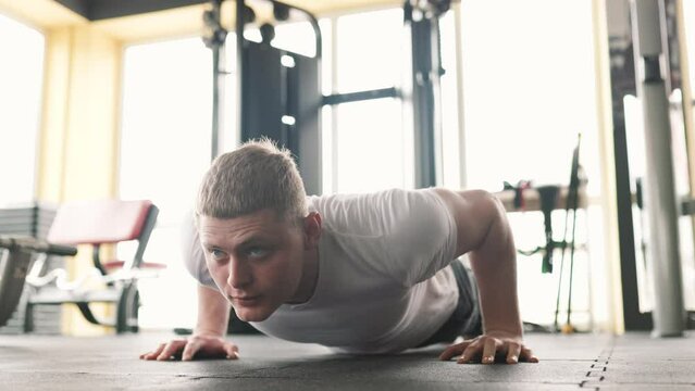 A determined young man performing pushups in a well-equipped gym during his intense training session. His strong and athletic physique showcases the power and strength he has developed