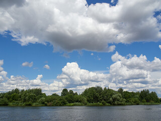 Summer landscape. Green Trees and clouds are reflected in the river. Beautiful sky with cumulus clouds.