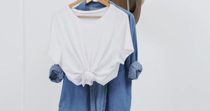 Video of white and denim t shirt on hangers, hat and copy space on white background