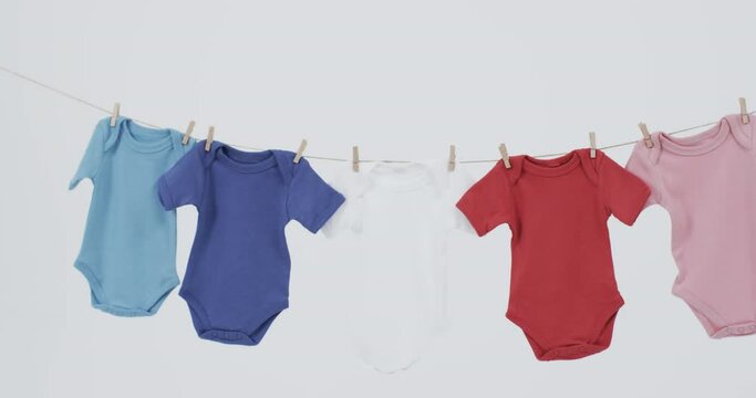 Video of multi coloured baby grows hanging on pegs from line with copy space on white background