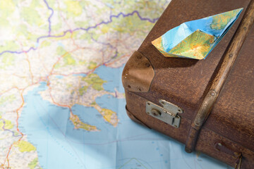 Folded paper boat on an old vintage suitcase placed on a map, travel, wanderlust and cruise...