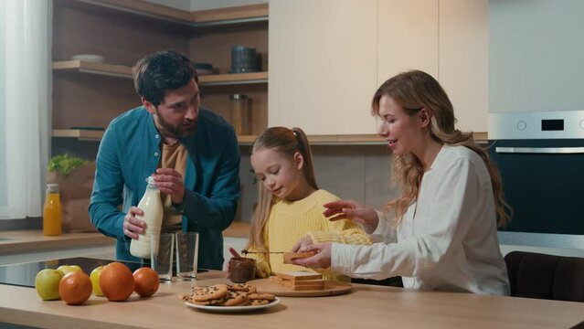 Caucasian happy family at kitchen morning breakfast with food delivery service parents mother father with child daughter kid girl cooking toasts bread with chocolate pasta dad pour milk into glasses