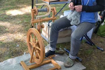 Woman spins raw wool into thread with a wooden spinning wheel at a, open air craft market, copy...