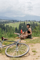 Fototapeta premium Young woman cyclist drink water from red bottle with view on carpathian mountains