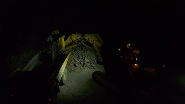 Loading the rock in dumper large quarry truck to transport ore from open-pit at night, slow motion