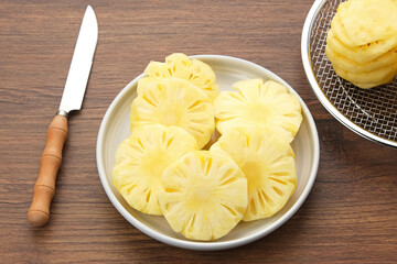 Fresh slices pineapple served in white plate on wooden table