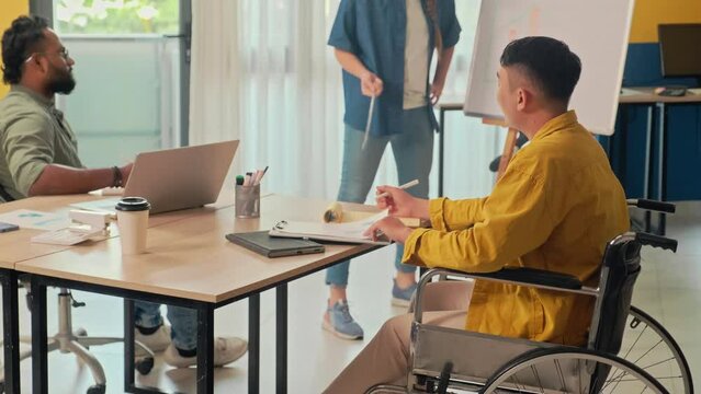 Medium shot of man in wheelchair having meeting with co-workers discussing work projects at office