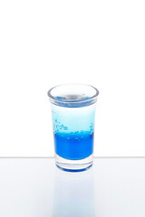 Blue cocktail in a shot glass on a mirror counter bar isolated on white background.