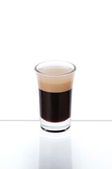 B-52 Cocktail in a shot glass on a mirror counter bar isolated on white background. Separation layer between Coffee liqueur, Irish cream Liqueur and Orange Cognac.