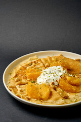 Crepes suzette with ice cream, nuts and oranges on a dark background.