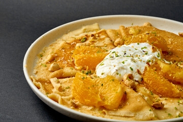Crepes suzette with ice cream, nuts and oranges on a dark background.